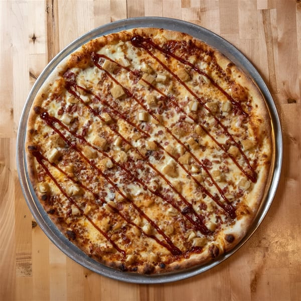 A BBQ chicken pizza from The NY Pizza Place, topped with chicken, bacon, and BBQ sauce drizzle.