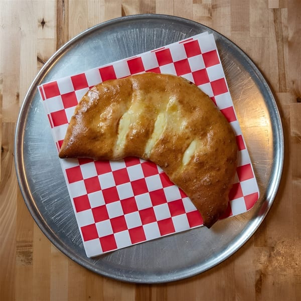 Golden-brown calzone with melted cheese, served on red and white checkered paper on a metal tray.