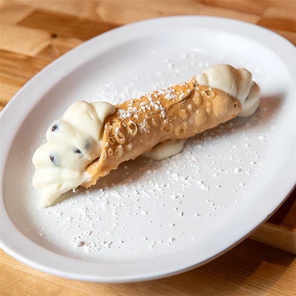 A cannoli from The NY Pizza Place, filled with creamy ricotta and chocolate chips, dusted with powdered sugar.