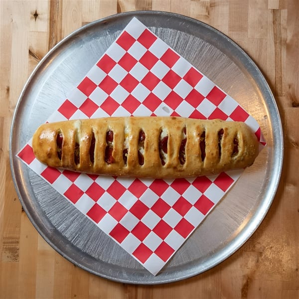 A golden-brown stromboli with visible pepperoni and cheese, served on red and white checkered paper.