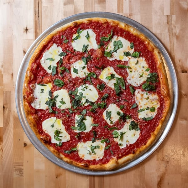 A freshly baked NY Pizza Place Margherita pizza with rich red sauce, mozzarella, and basil on a wooden table.