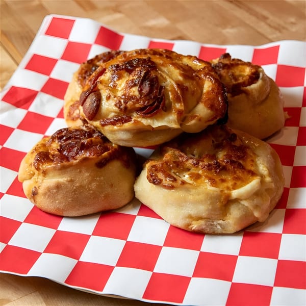 Four golden-brown pepperoni and cheese rolls on red and white checkered paper from The NY Pizza Place.