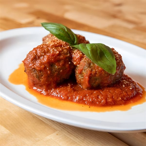 Three meatballs covered in red sauce, parmesan, and basil on a white plate.