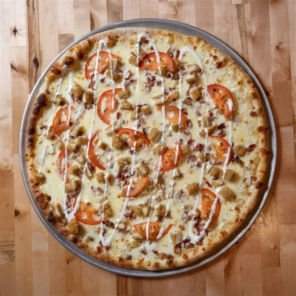 A NY Pizza Place pizza with white sauce, chicken, bacon, tomatoes, and a ranch drizzle.