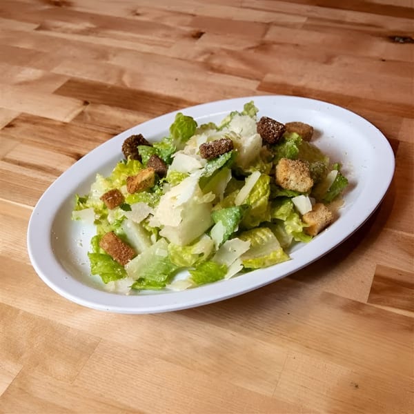 A Caesar salad with romaine lettuce, croutons, and parmesan cheese on a white oval plate.