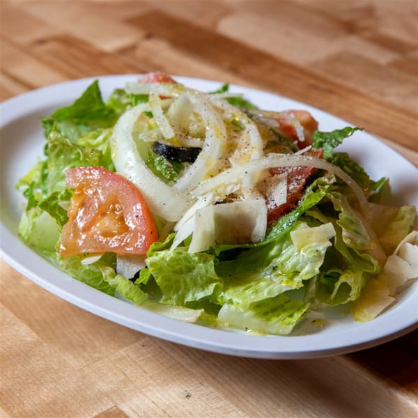 A fresh garden salad with lettuce, tomatoes, onions, olives, and shaved cheese on a white plate.