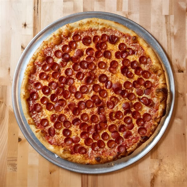 A large, round pepperoni pizza on a metal tray, centered on a light wooden table.