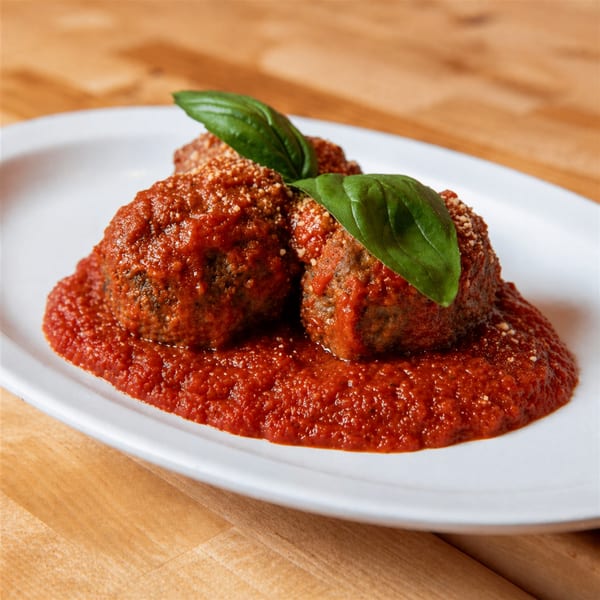 Three meatballs covered in red sauce, sprinkled with cheese, and garnished with basil on a white plate.