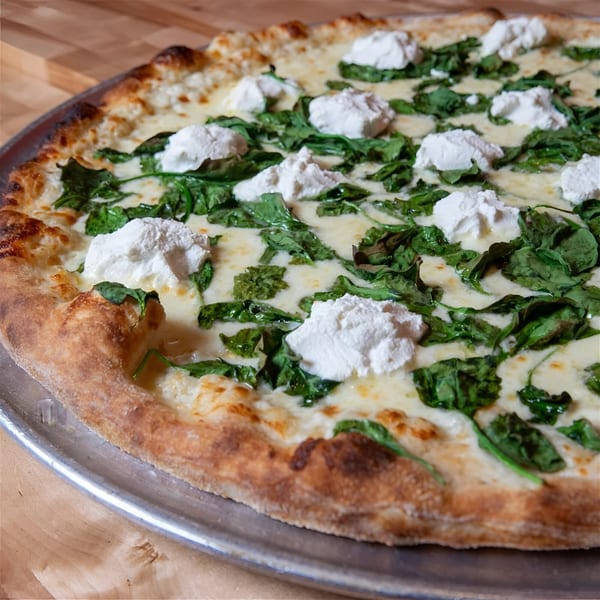 The NY Pizza Place's white pizza with spinach and dollops of ricotta cheese on a metal pan.